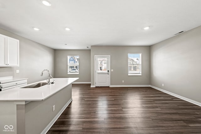 kitchen featuring a center island with sink, white cabinets, dark wood-style flooring, light countertops, and a sink