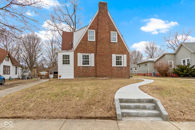 view of front facade with brick siding, a front lawn, and a chimney