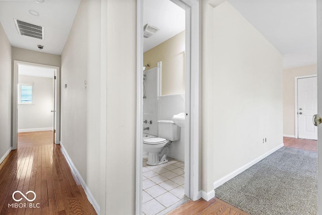 hallway with wood finished floors, visible vents, and baseboards