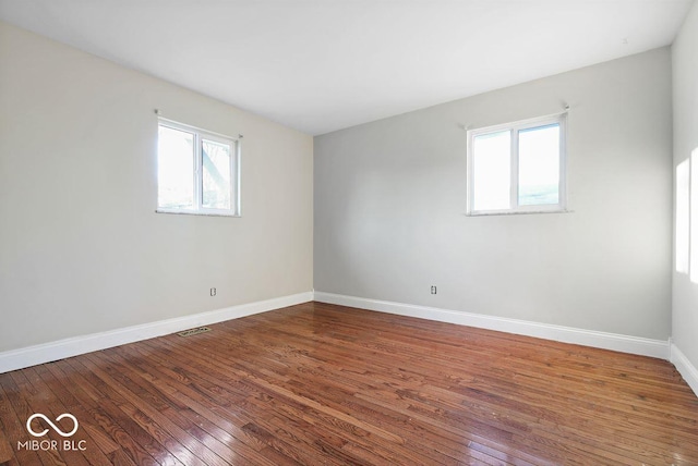 unfurnished room featuring wood-type flooring, visible vents, and baseboards