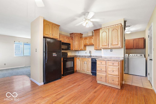 kitchen with washing machine and clothes dryer, light countertops, light wood-type flooring, black appliances, and a sink