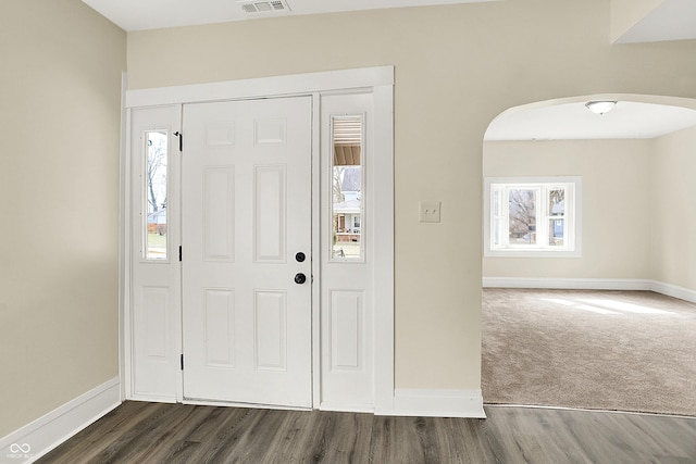 foyer with arched walkways, dark wood-type flooring, and baseboards