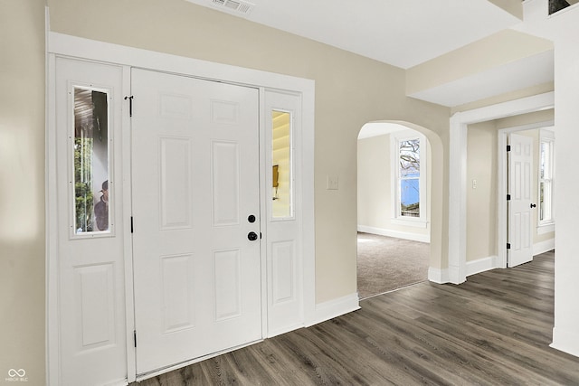 entryway with arched walkways, dark wood-type flooring, visible vents, and baseboards