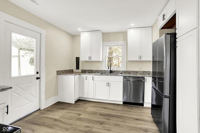 kitchen with stainless steel appliances, stone countertops, white cabinetry, a sink, and light wood-type flooring