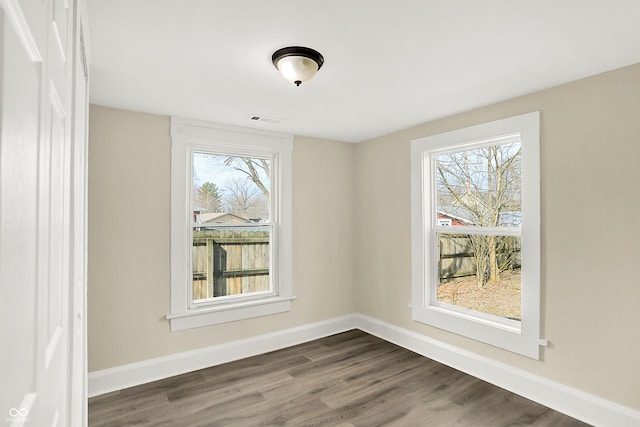 empty room featuring dark wood-type flooring, a wealth of natural light, visible vents, and baseboards