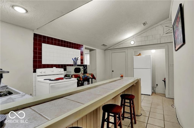 kitchen featuring white appliances, light tile patterned floors, tile countertops, vaulted ceiling, and a textured ceiling