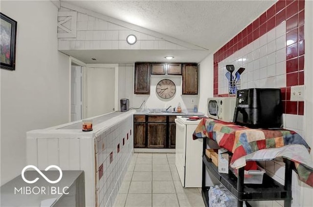 kitchen featuring white appliances, light tile patterned floors, lofted ceiling, dark brown cabinets, and a textured ceiling