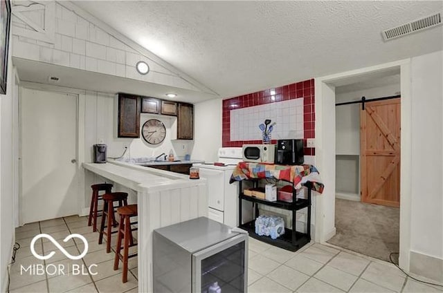 kitchen featuring light countertops, visible vents, a barn door, vaulted ceiling, and a textured ceiling