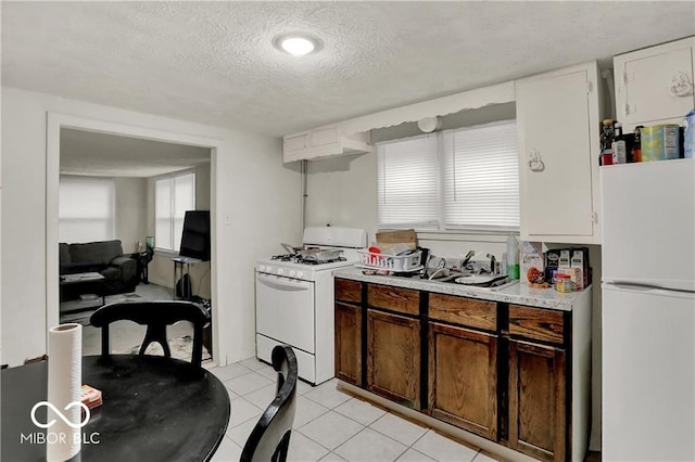 kitchen with a textured ceiling, light tile patterned flooring, white appliances, a sink, and light countertops