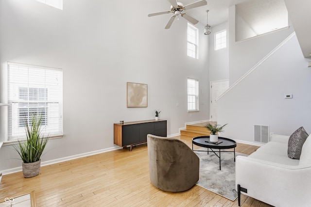 living room featuring light wood-type flooring, visible vents, a towering ceiling, baseboards, and ceiling fan