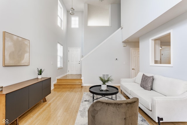 living area featuring stairway, light wood-style flooring, baseboards, and a healthy amount of sunlight