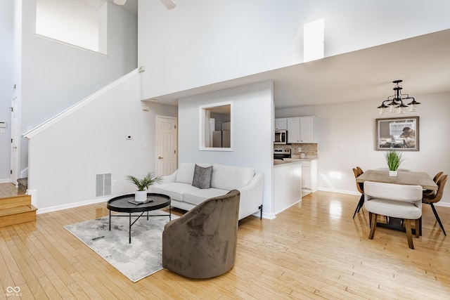 living room featuring baseboards, visible vents, stairs, light wood-style floors, and a chandelier