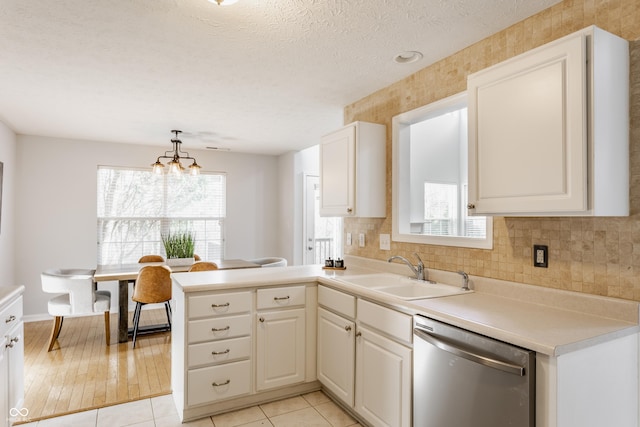 kitchen featuring a sink, stainless steel dishwasher, a textured ceiling, a peninsula, and decorative backsplash