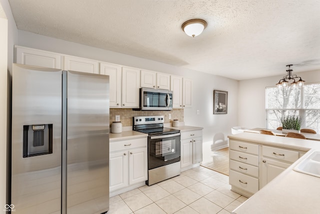 kitchen with tasteful backsplash, light countertops, a notable chandelier, white cabinets, and stainless steel appliances