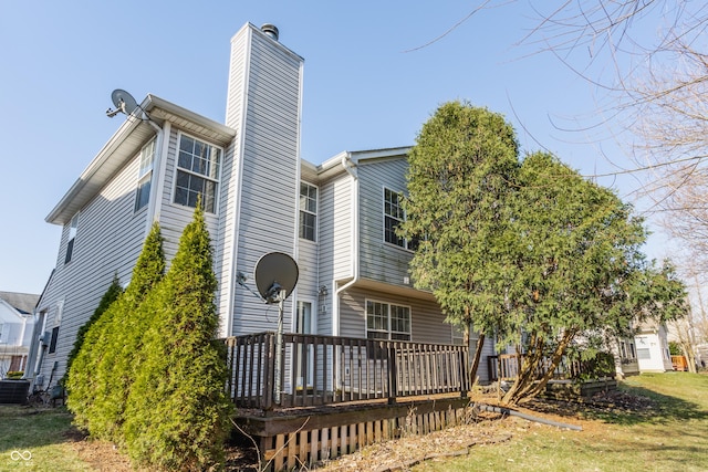 rear view of property featuring a chimney, a lawn, and a wooden deck