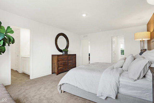 bedroom with light carpet, visible vents, baseboards, and ensuite bathroom