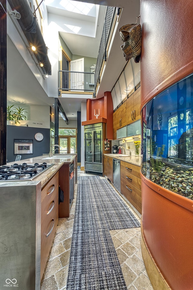 kitchen featuring stone tile floors, brown cabinetry, a skylight, appliances with stainless steel finishes, and a towering ceiling