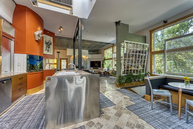 kitchen featuring a sink, stone tile flooring, dishwasher, open floor plan, and backsplash