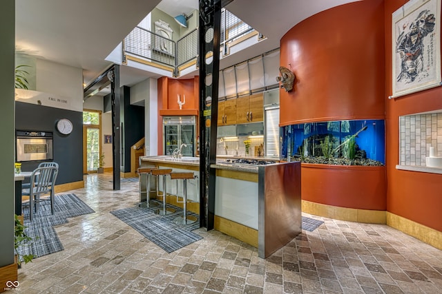 bar with oven, a sink, a high ceiling, brick floor, and baseboards