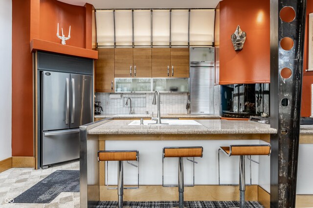 kitchen with decorative backsplash, light stone countertops, a kitchen bar, and freestanding refrigerator