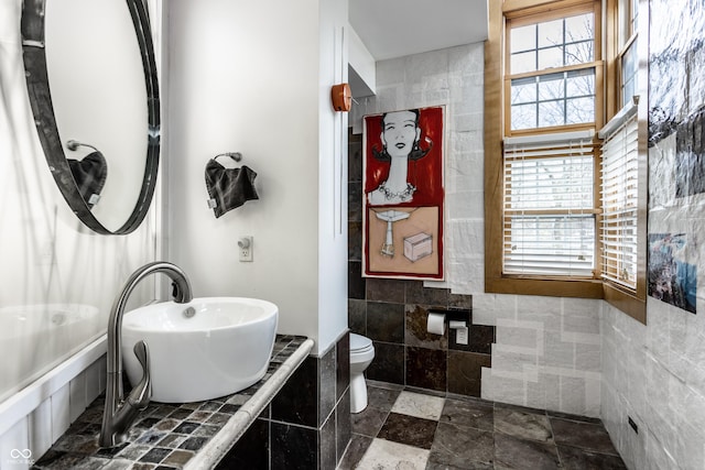 bathroom with a sink, tile walls, toilet, and stone tile flooring