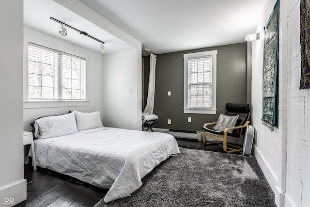 bedroom featuring a baseboard heating unit, baseboards, track lighting, and dark wood-style flooring