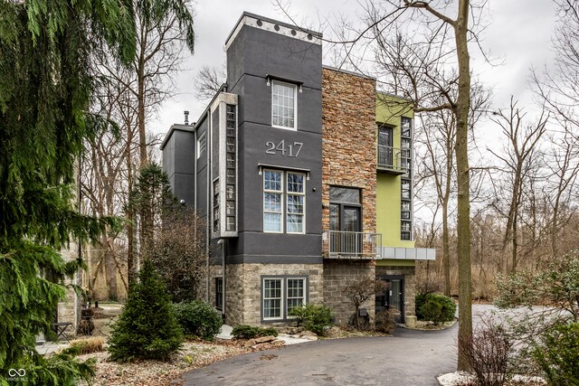 view of front of property featuring aphalt driveway, stone siding, and stucco siding