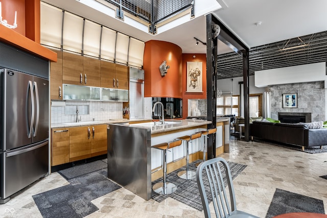 kitchen with backsplash, stainless steel built in fridge, brown cabinets, a fireplace, and a towering ceiling