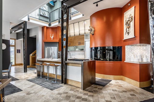 kitchen with baseboards, tasteful backsplash, a towering ceiling, and stainless steel refrigerator