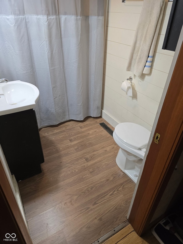 bathroom with wooden walls, a shower with shower curtain, toilet, wood finished floors, and vanity