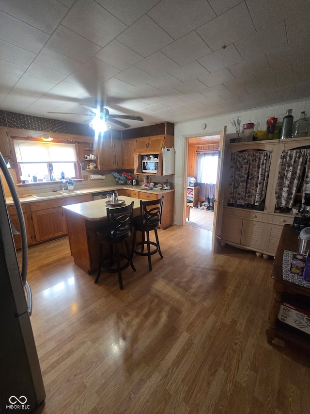 kitchen featuring a breakfast bar area, brown cabinets, freestanding refrigerator, light countertops, and light wood-type flooring