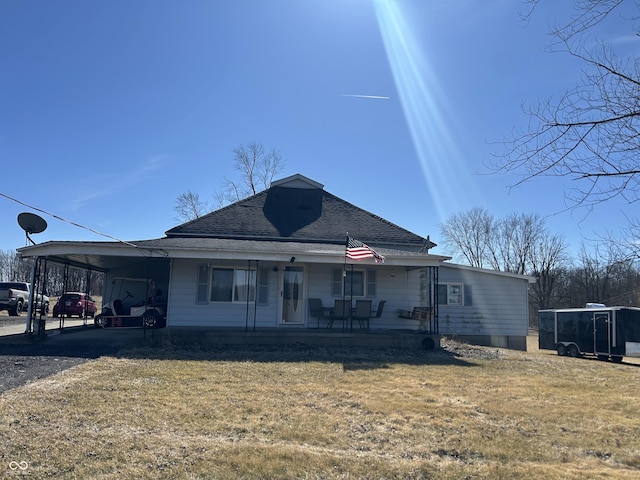 view of front facade with an attached carport, covered porch, a shingled roof, driveway, and a front lawn