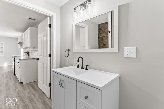 bathroom with visible vents, vanity, decorative backsplash, and wood finished floors