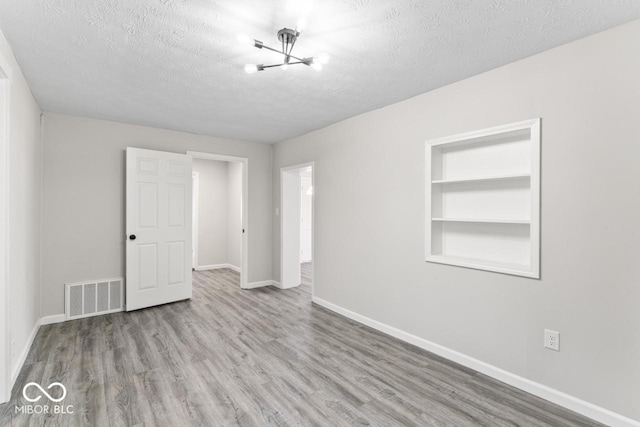 unfurnished room featuring built in shelves, visible vents, a textured ceiling, wood finished floors, and baseboards