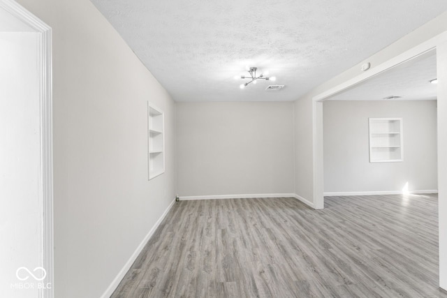 empty room with built in features, a textured ceiling, and baseboards