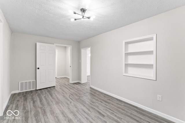 unfurnished room with baseboards, visible vents, wood finished floors, a textured ceiling, and built in shelves