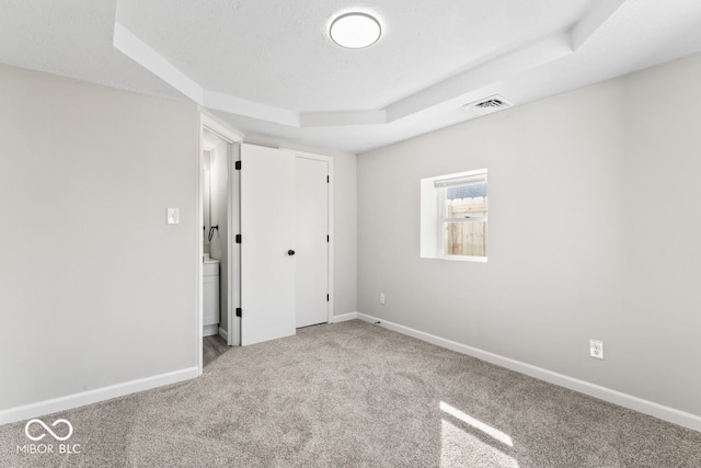 unfurnished bedroom with a textured ceiling, carpet floors, visible vents, baseboards, and a tray ceiling