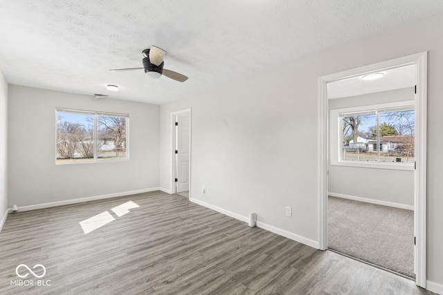 unfurnished bedroom featuring a textured ceiling, multiple windows, wood finished floors, and baseboards