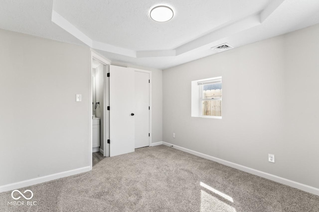 unfurnished bedroom with a textured ceiling, visible vents, baseboards, carpet, and a raised ceiling