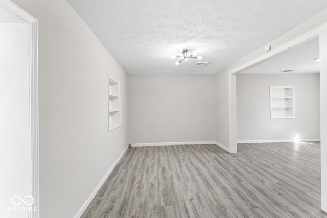 unfurnished room featuring built in features, visible vents, a textured ceiling, wood finished floors, and baseboards