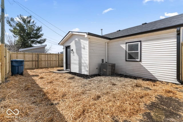 rear view of property with a shingled roof, fence, and central AC unit