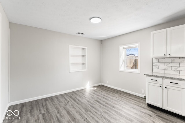 unfurnished dining area with a textured ceiling, built in shelves, light wood-style flooring, visible vents, and baseboards