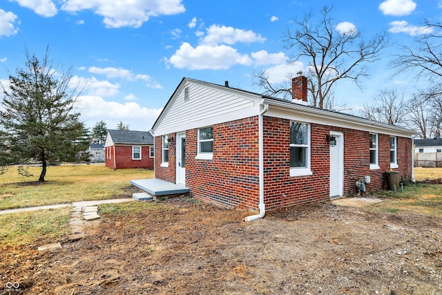 view of property exterior with a yard, brick siding, a chimney, and an outdoor structure