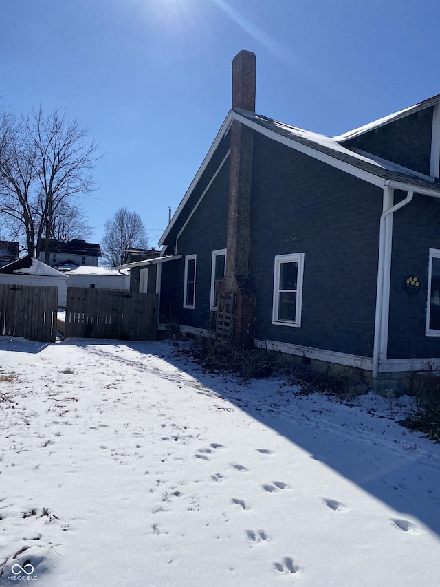 view of snowy exterior with a chimney and fence