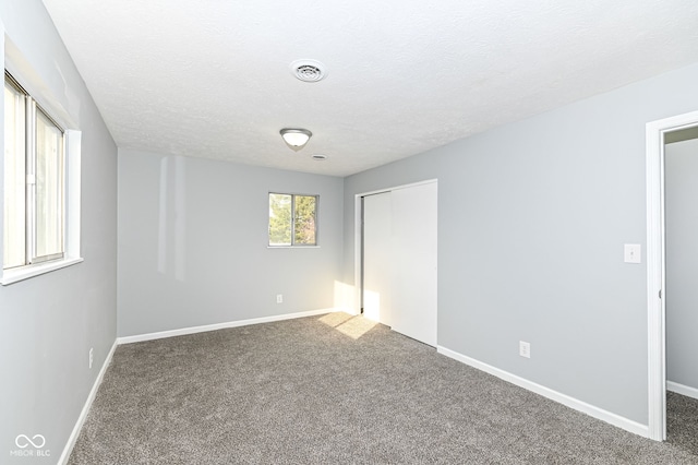 carpeted empty room featuring a textured ceiling, visible vents, and baseboards