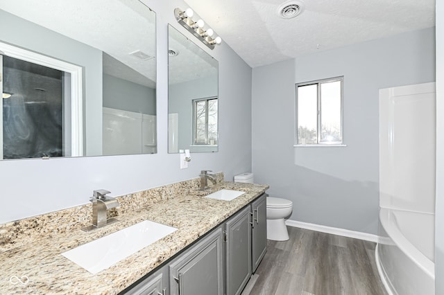 bathroom with a textured ceiling, visible vents, a sink, and wood finished floors