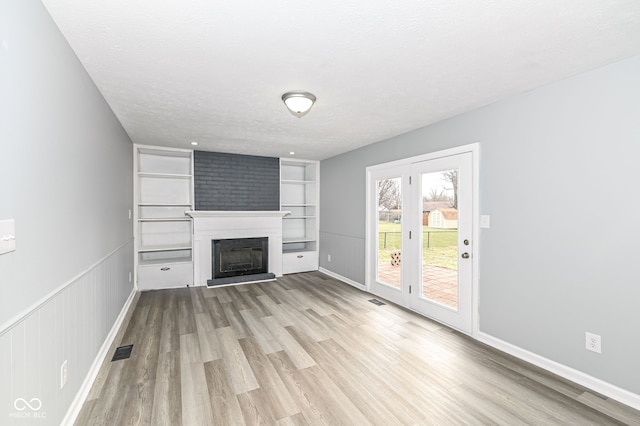 unfurnished living room featuring built in shelves, a fireplace, visible vents, a textured ceiling, and wood finished floors