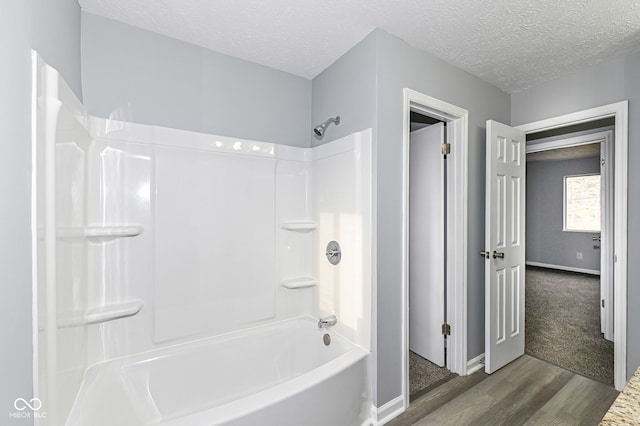 bathroom with a textured ceiling, bathtub / shower combination, wood finished floors, and baseboards