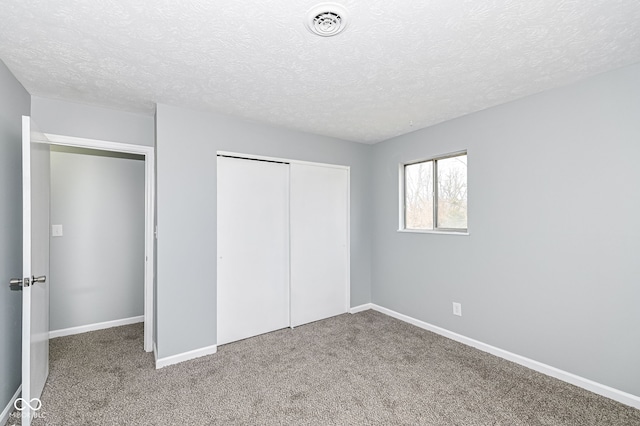 unfurnished bedroom with a closet, visible vents, carpet flooring, a textured ceiling, and baseboards