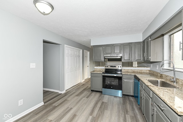 kitchen featuring under cabinet range hood, gray cabinetry, a sink, dishwasher, and stainless steel range with electric stovetop